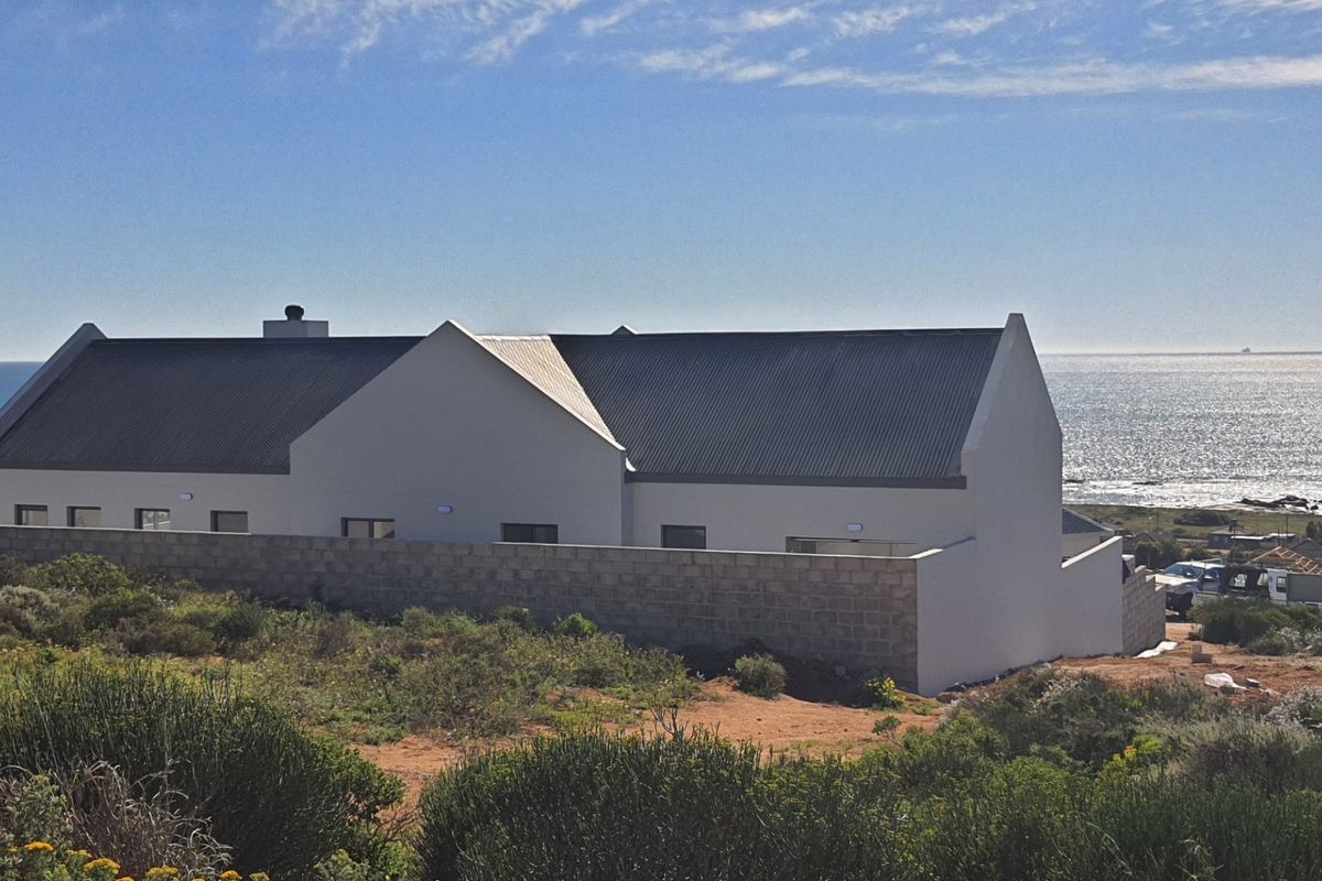 Rear view of a modern coastal home featuring a corrugated metal roof and a masonry boundary wall overlooking the ocean.