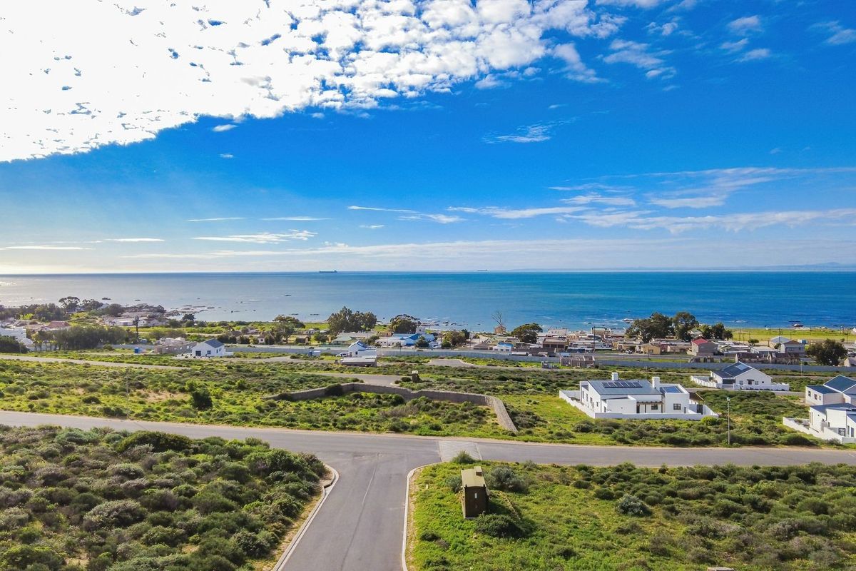 An aerial view of a coastal residential area featuring paved roads, established housing, and expansive ocean views under a clear sky.