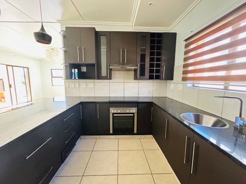 Modern kitchen featuring dark cabinetry, granite countertops, built-in oven, extractor fan, and tiled flooring in a clean, well-maintained space.