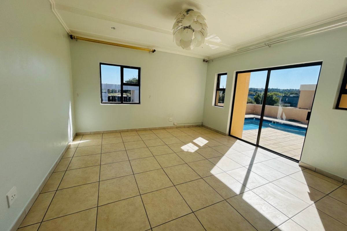 A bright, empty living room featuring tiled flooring and large sliding glass doors that provide direct access to the outdoor pool area.