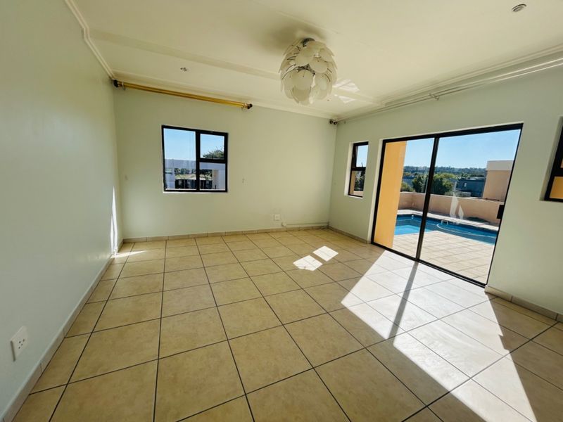 A bright, empty living room featuring tiled flooring and large sliding glass doors that provide direct access to the outdoor pool area.