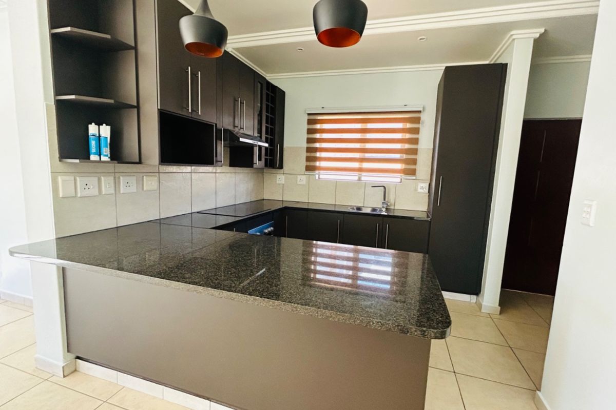 Modern kitchen featuring dark cabinetry, granite countertops, tiled backsplash, and integrated lighting, offering a clean and functional workspace.