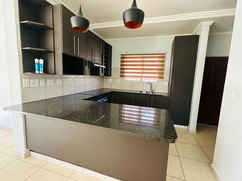 Modern kitchen featuring dark cabinetry, granite countertops, tiled backsplash, and integrated lighting, offering a clean and functional workspace.