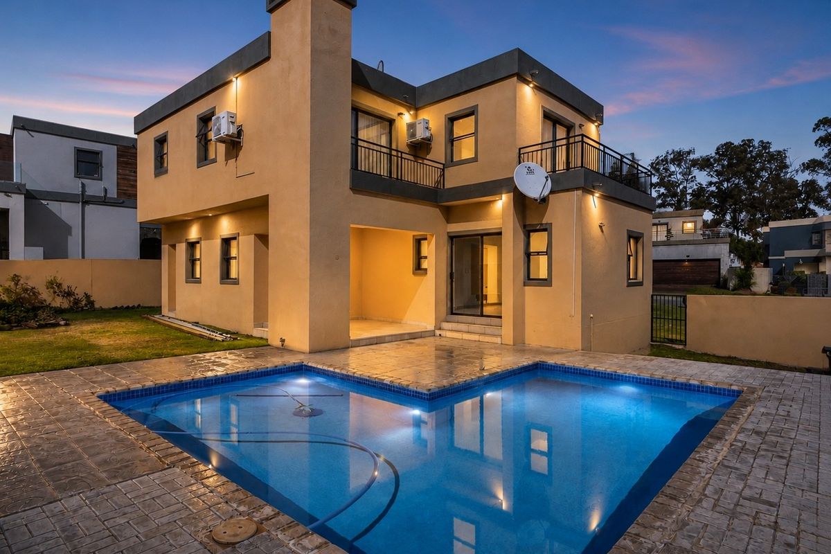 Rear view of a modern two-story house featuring a swimming pool, paved patio area, and an upper-level balcony at dusk.