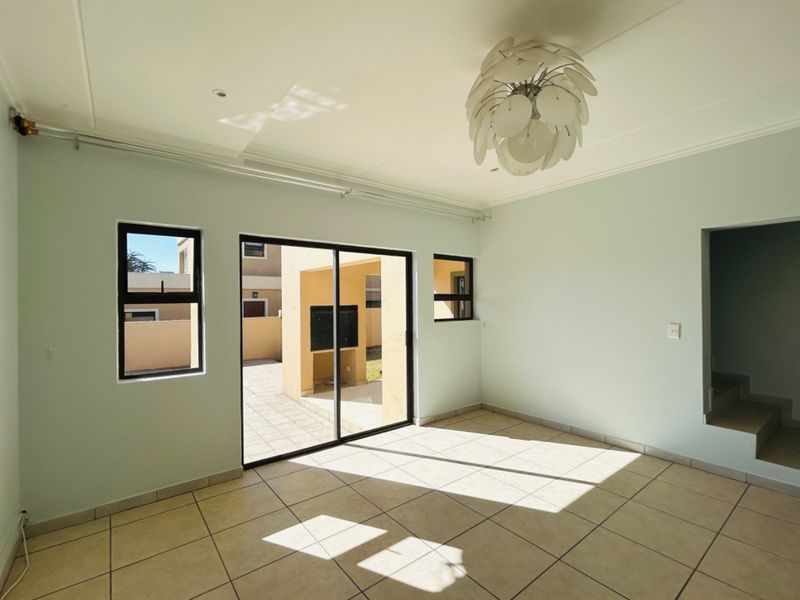 A bright, empty living room featuring neutral tiled flooring, large sliding glass doors leading to an outdoor patio, and modern aluminium window frames.