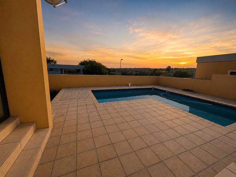 An outdoor pool area featuring a tiled deck and perimeter wall, offering elevated views at sunset.