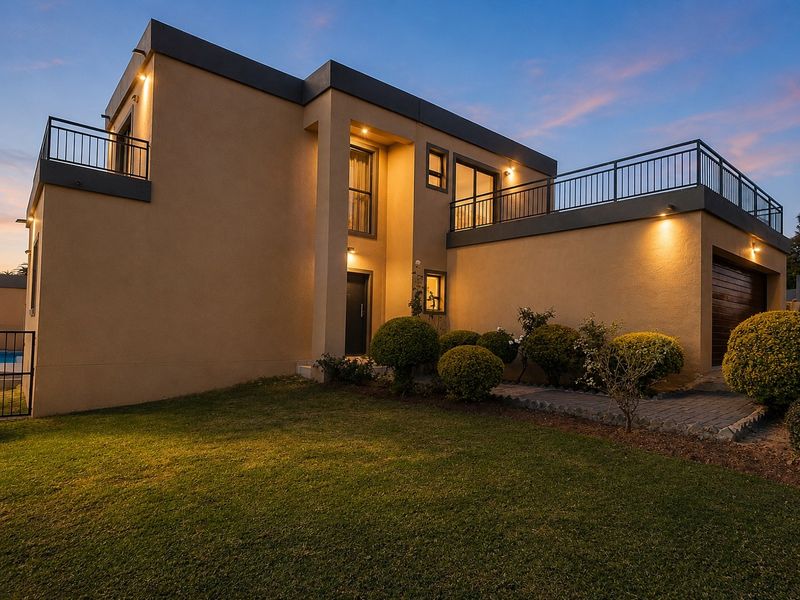 Rear view of a modern two-story house featuring a spacious upper-level balcony, integrated garage, and well-maintained garden area at dusk.