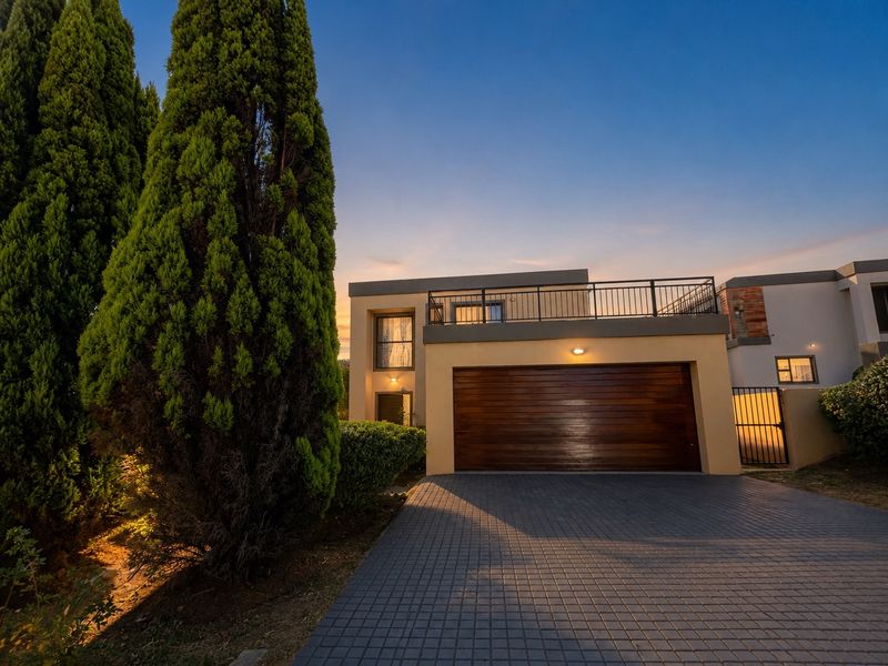 Front elevation of a modern house featuring a paved driveway, timber garage door, and an upper-level balcony with metal balustrade.