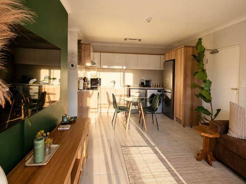 A bright open-plan living and kitchen area featuring modern wood-finish cabinetry, tiled floors, and integrated appliances in a well-maintained apartment setting.
