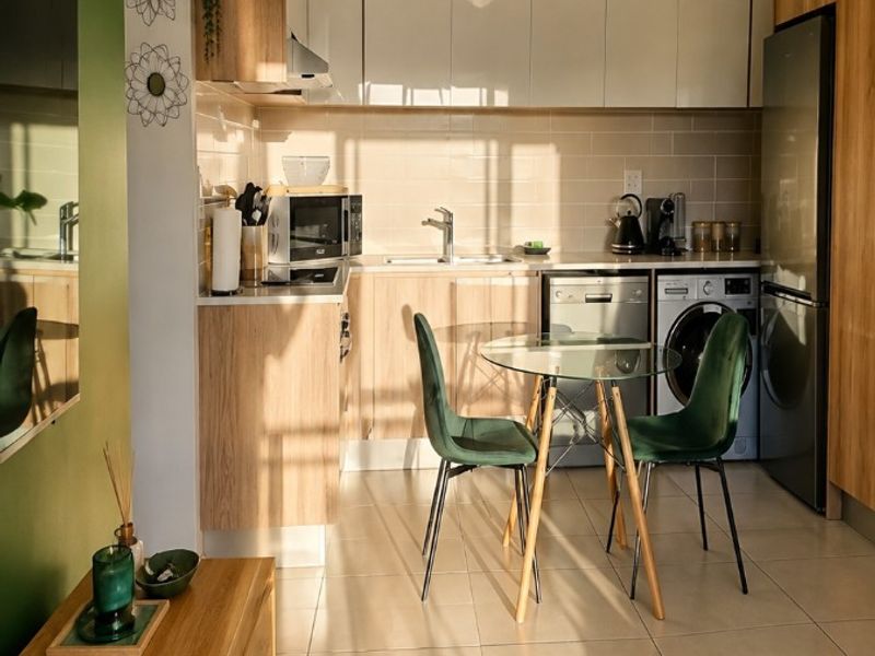A modern open-plan kitchen featuring light wood cabinetry, tiled flooring, integrated appliances, and a neutral backsplash, creating a bright and functional living space.