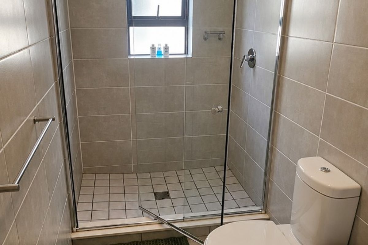 A clean and modern bathroom featuring a walk-in shower with a glass enclosure, neutral wall and floor tiling, and a standard toilet.