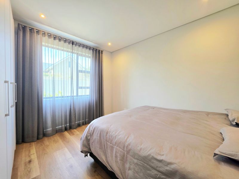 A bright and modern bedroom featuring light laminate flooring, built-in cupboards, and recessed downlighting.
