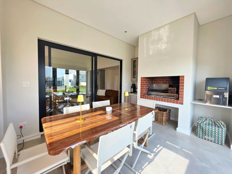 A modern covered patio featuring a built-in brick braai, large sliding glass doors, and neutral tiled flooring, perfect for outdoor entertaining.