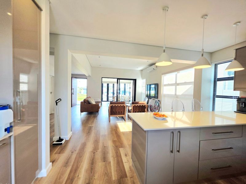 Modern open-plan living area featuring a sleek kitchen island with quartz countertops, pendant lighting, and seamless flow to the outdoor patio through sliding doors.