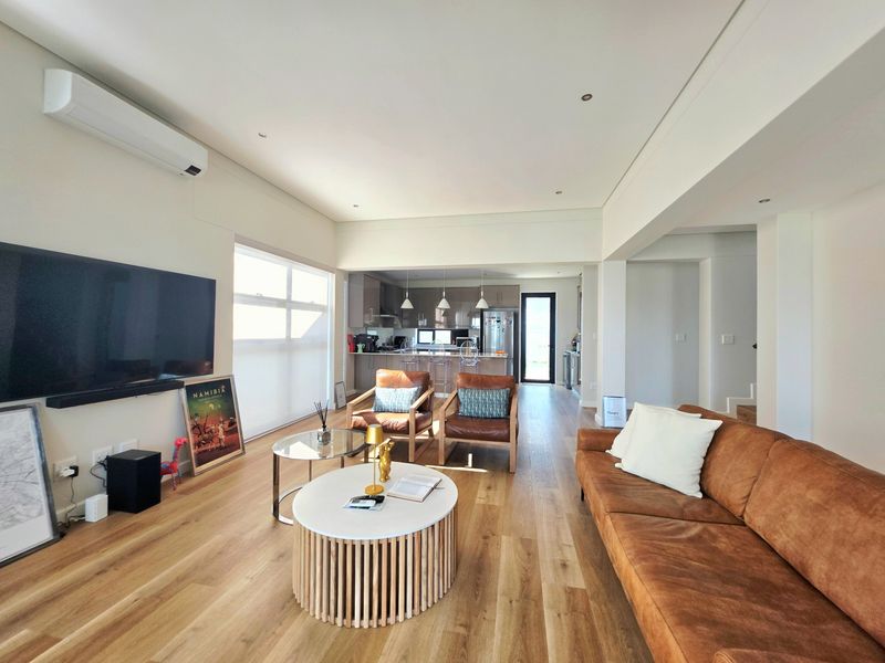 Spacious open-plan living area featuring timber flooring, recessed lighting, and a modern kitchen with a central island and sleek cabinetry.