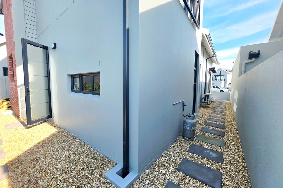 A well-maintained side exterior passage featuring a stone pathway, gravel landscaping, and modern grey rendered walls with integrated drainage.