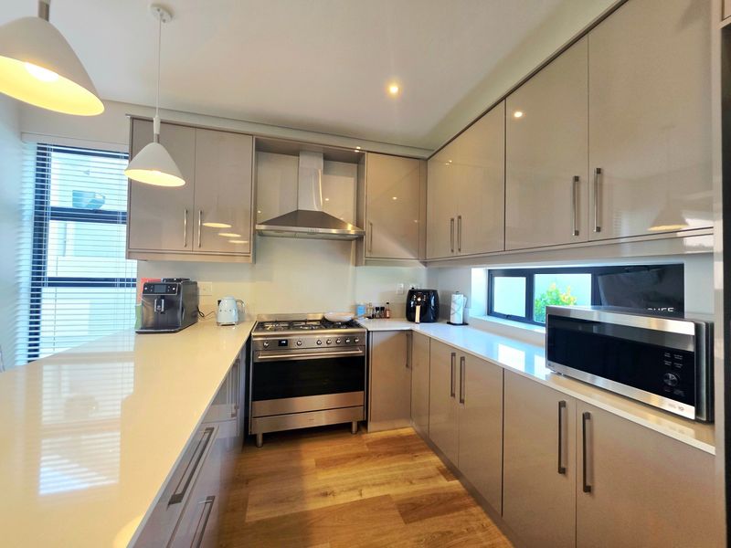 Modern kitchen featuring high-gloss cabinetry, quartz countertops, stainless steel gas oven, extractor fan, and built-in microwave with contemporary pendant lighting.