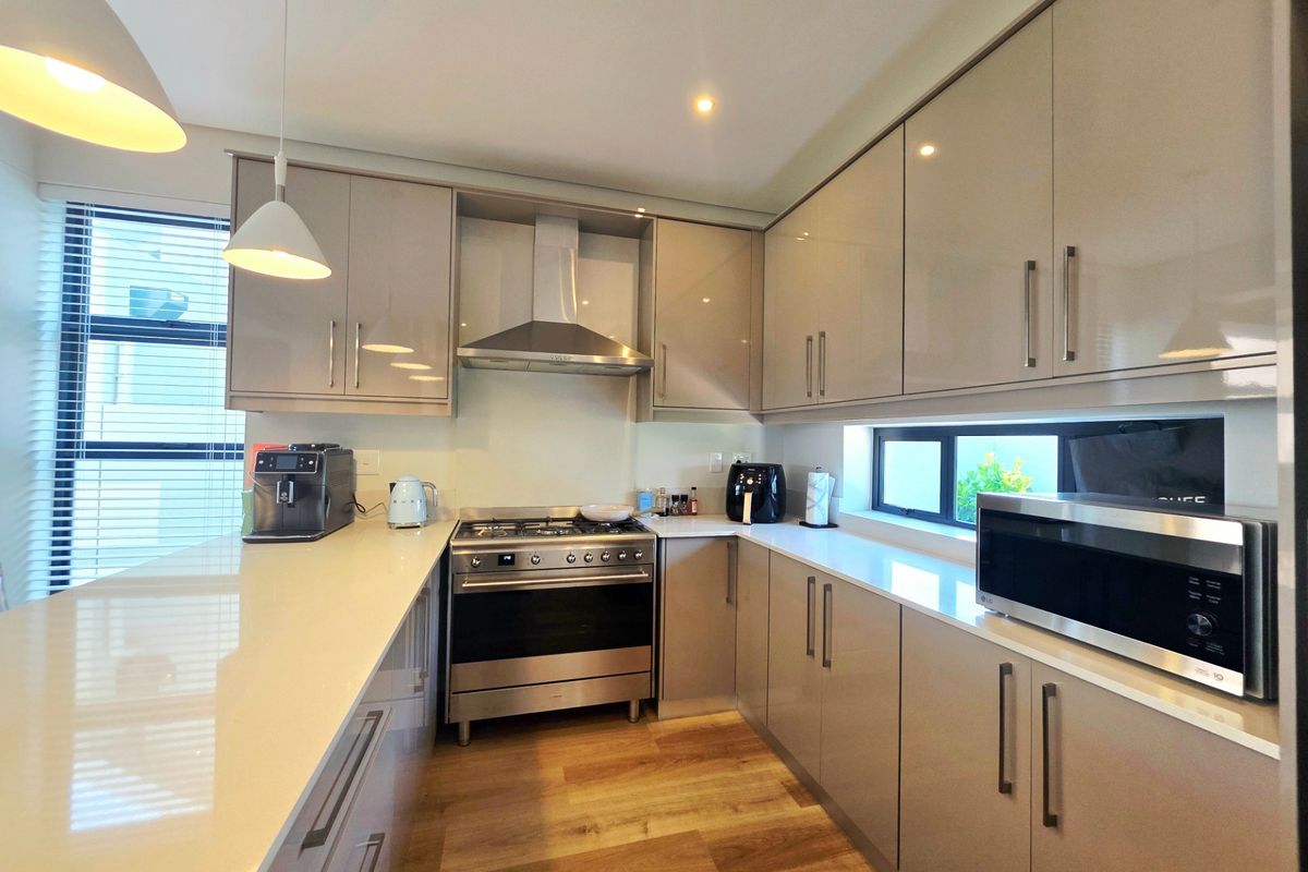 Modern kitchen featuring high-gloss cabinetry, quartz countertops, stainless steel gas oven, extractor fan, and built-in microwave with contemporary pendant lighting.