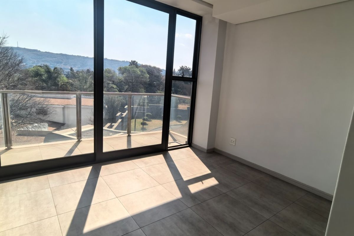 A bright, empty living area featuring large sliding glass doors that open onto a balcony with scenic views and modern tiled flooring.