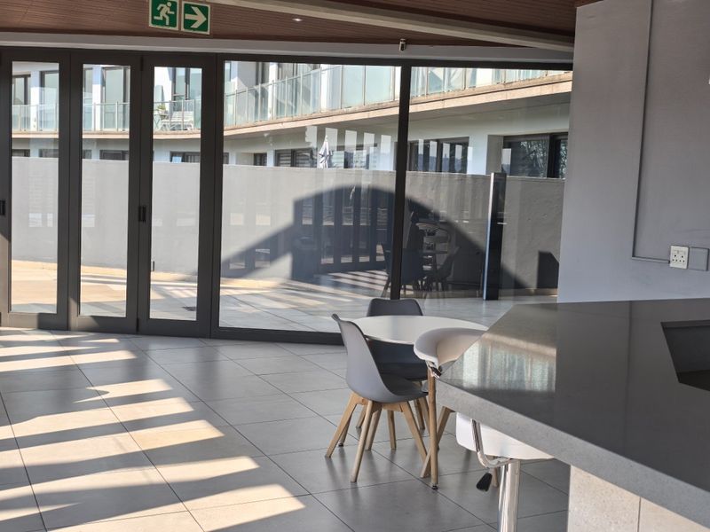Modern open-plan living area featuring large bi-fold glass doors that open to an outdoor space, complemented by a stone-topped breakfast bar and tiled flooring.