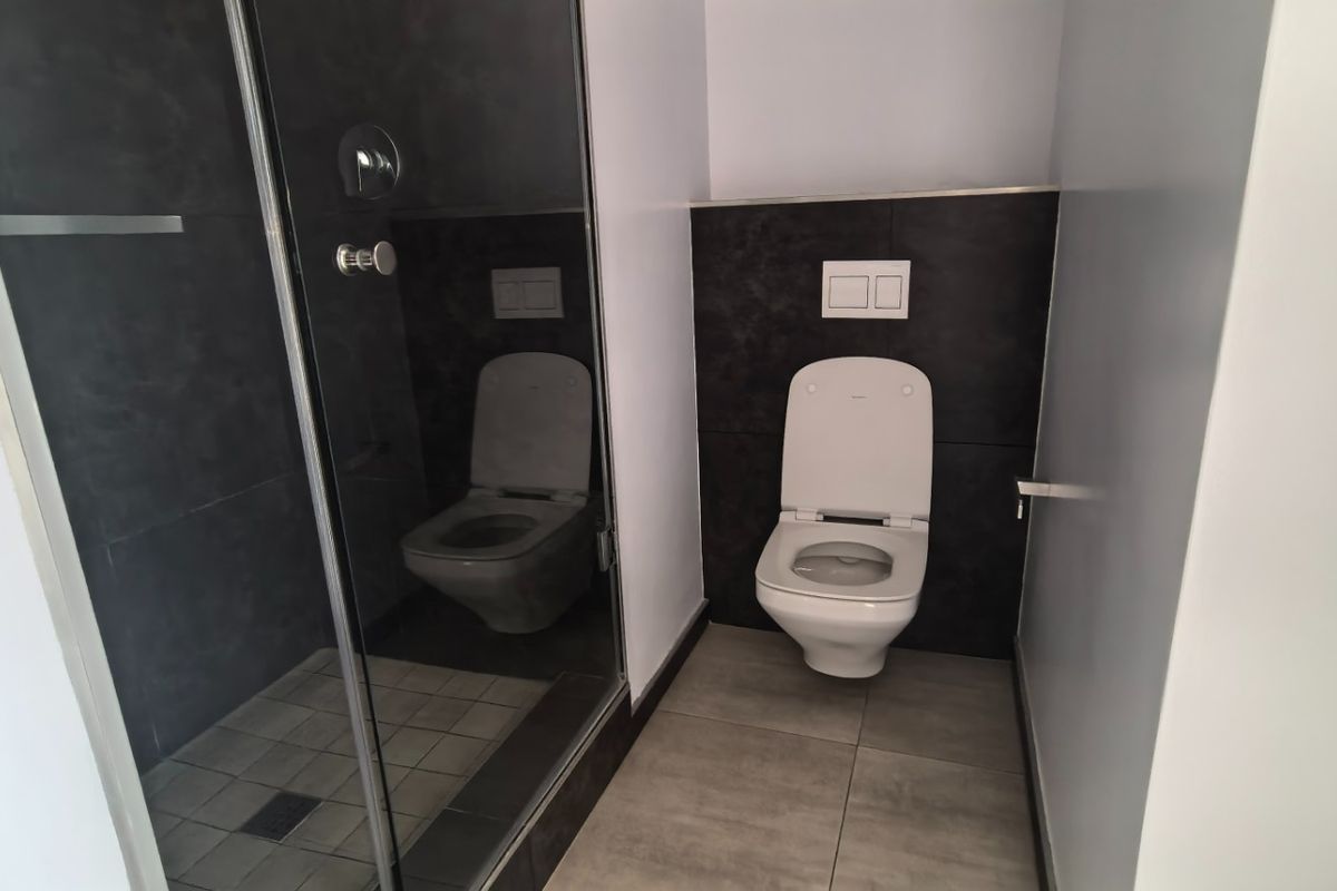 Modern bathroom featuring a walk-in shower with glass enclosure and a wall-mounted toilet with contemporary dark tile accents.