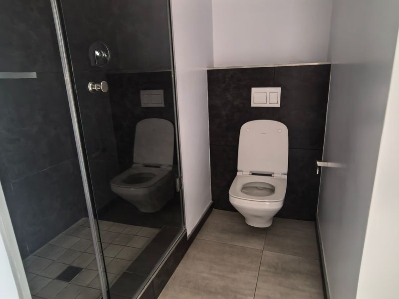 Modern bathroom featuring a walk-in shower with glass enclosure and a wall-mounted toilet with contemporary dark tile accents.