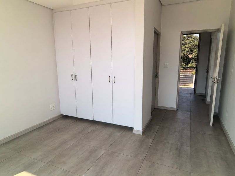A bright, empty bedroom featuring neutral tiled flooring and ample built-in cupboard storage, leading to an adjacent hallway.