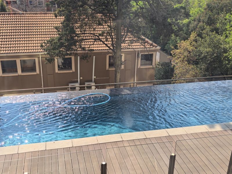 An elevated infinity edge swimming pool featuring modern composite decking and a sleek glass balustrade, offering a clear view of the surrounding landscape.