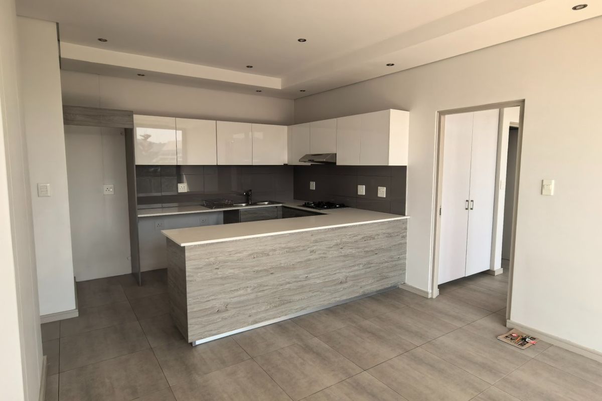 Modern open-plan kitchen featuring sleek white cabinetry, wood-grain breakfast bar, stone countertops, and integrated hob with extractor fan, set on neutral tiled flooring.