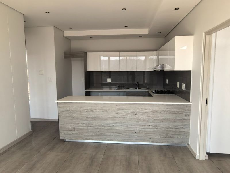 Modern open-plan kitchen featuring sleek white cabinetry, wood-grain island finish, stone countertops, and integrated hob with extractor fan in a bright, tiled space.