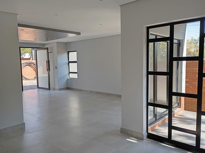 A bright, modern, and spacious open-plan living area featuring neutral tiled floors, recessed lighting, and large black-framed glass doors leading to the exterior.