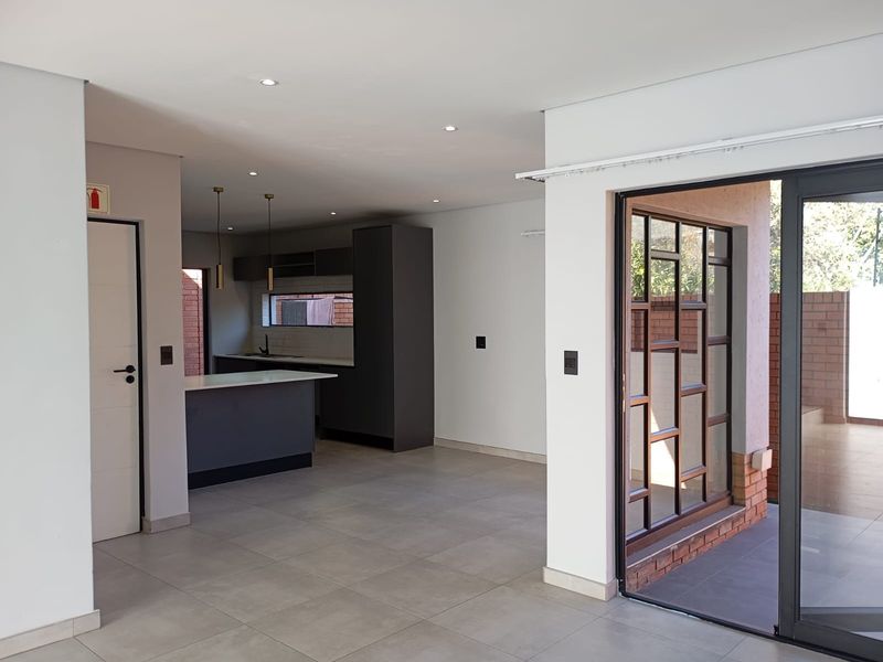 Modern open-plan living and kitchen area featuring sleek dark cabinetry, a central island, tiled floors, and seamless access to an outdoor patio space.