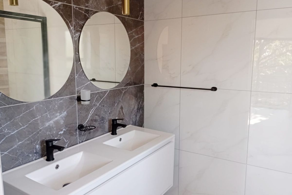 Modern bathroom featuring a sleek double vanity with black fixtures, contrasting marble-look wall tiles, and contemporary circular mirrors.