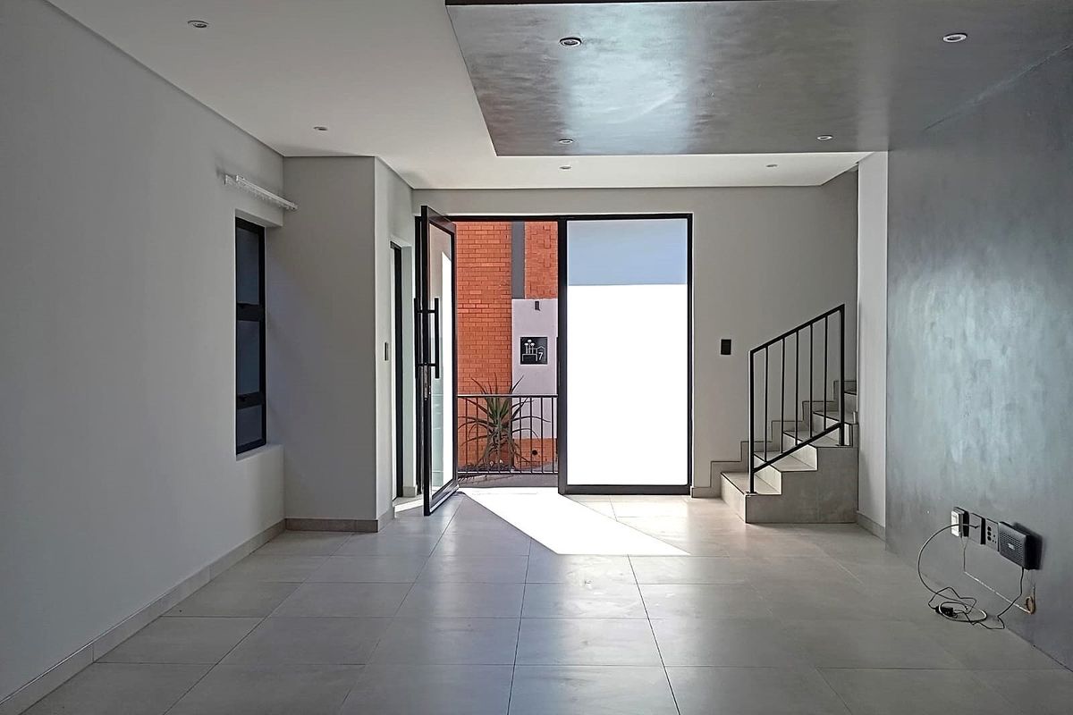 Spacious, modern open-plan living area featuring large format floor tiles, a striking metallic feature wall, and a contemporary staircase with a sleek metal railing.