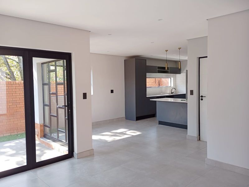 Modern open-plan living area featuring a sleek kitchen with dark cabinetry, a central island, and seamless access to the outdoor patio through sliding doors.