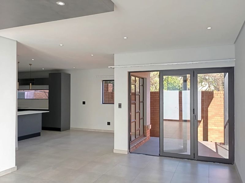 Spacious open-plan living area featuring modern tiled floors, recessed lighting, and seamless access to an outdoor patio through aluminium stacker doors.