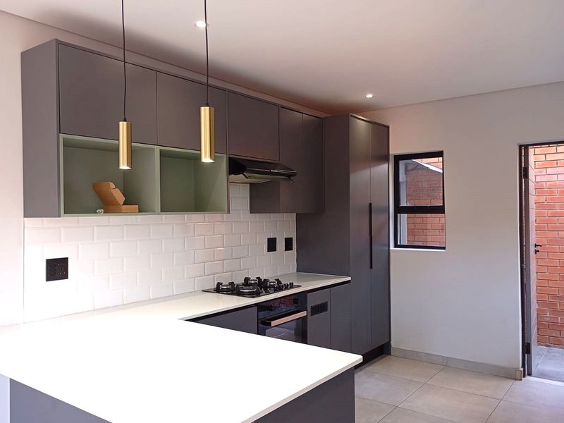 Modern kitchen featuring sleek grey cabinetry, white stone countertops, subway tile backsplash, integrated gas hob, and built-in oven with contemporary pendant lighting.