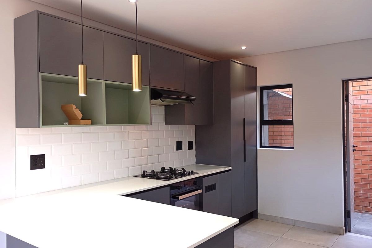Modern kitchen featuring sleek grey cabinetry, white stone countertops, subway tile backsplash, integrated gas hob, and built-in oven with contemporary pendant lighting.