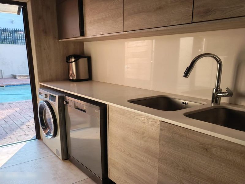 A modern, well-maintained scullery featuring sleek laminate cabinetry, stone countertops, a double basin sink, and direct access to the outdoor pool area.