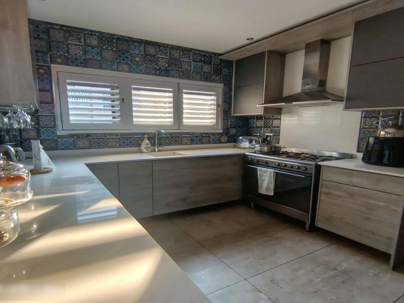 Modern kitchen featuring wood-finish cabinetry, stone countertops, a gas stove with extractor fan, and a decorative tiled backsplash.