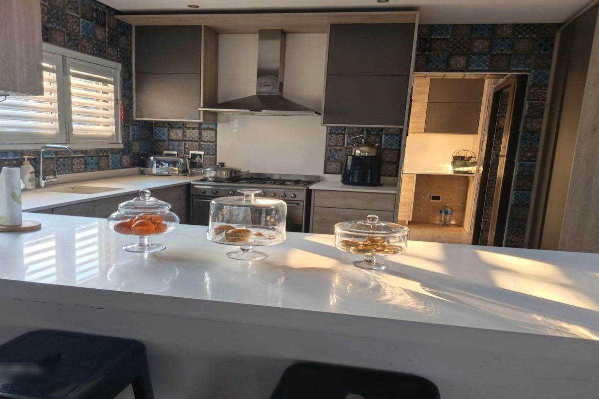 Modern kitchen featuring a white quartz breakfast bar, gas stove with extractor fan, and decorative tiled backsplash, with an adjacent scullery area.