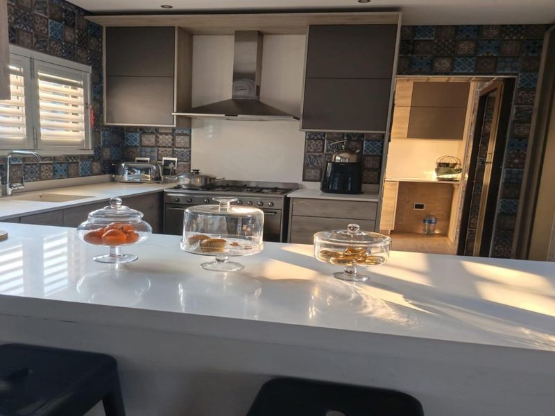 Modern kitchen featuring a white quartz breakfast bar, gas stove with extractor fan, and decorative tiled backsplash, with an adjacent scullery area.