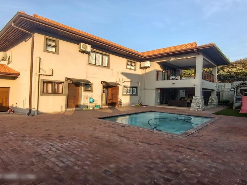 Rear exterior view of the townhouse featuring a paved patio area, swimming pool, and a covered upper-level balcony.