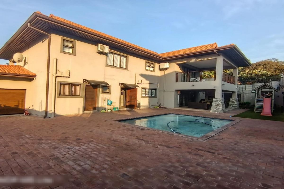 Rear exterior view of the townhouse featuring a paved patio area, swimming pool, and a covered upper-level balcony.