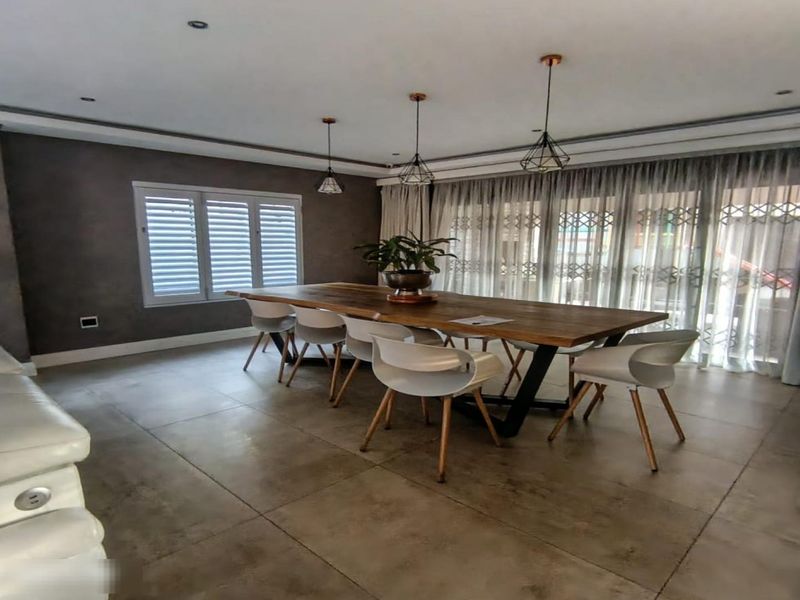 Spacious dining area featuring large format floor tiles, modern pendant lighting, and plantation shutters, with direct access to the outdoor area via sliding doors.