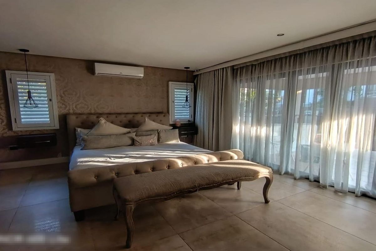 Spacious bedroom featuring tiled flooring, split-system air conditioning, recessed lighting, and large sliding glass doors leading to an outdoor area with plantation shutters.