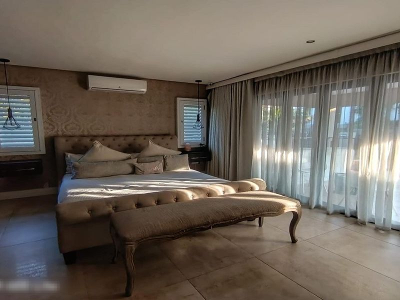 Spacious bedroom featuring tiled flooring, split-system air conditioning, recessed lighting, and large sliding glass doors leading to an outdoor area with plantation shutters.