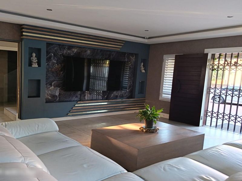 Spacious living room featuring a modern built-in media wall, recessed downlighting, and tiled flooring with direct access to the exterior through a security gate.