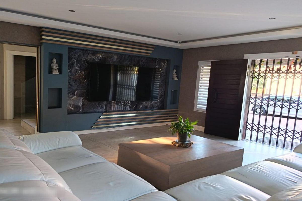 Spacious living room featuring a modern built-in media wall, recessed downlighting, and tiled flooring with direct access to the exterior through a security gate.