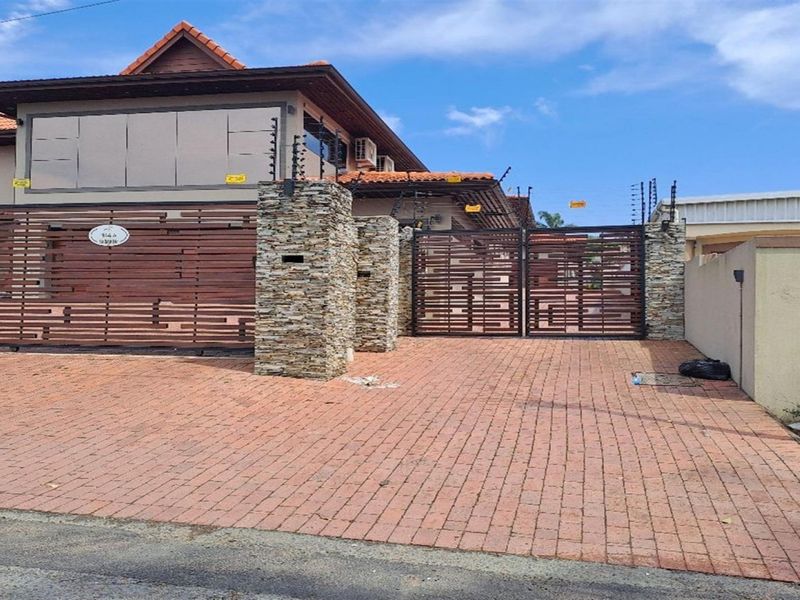 Front elevation of the townhouse featuring a brick paved driveway, stone-clad pillars, and secure horizontal slat gates with integrated electric fencing.